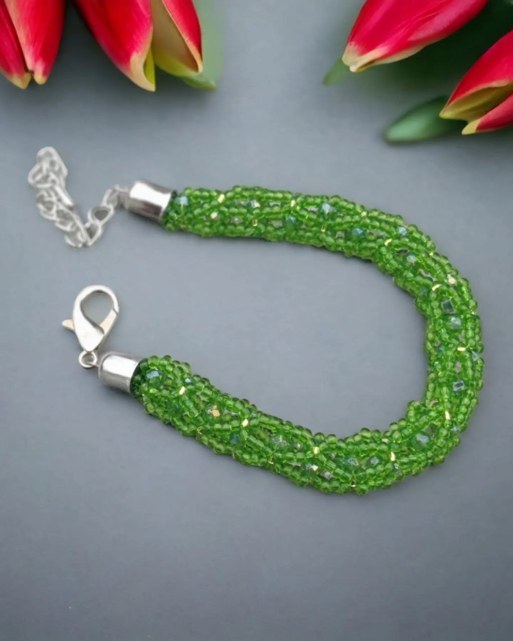 Close-up of green beaded bracelet with silver-plated lobster clasp on grey background