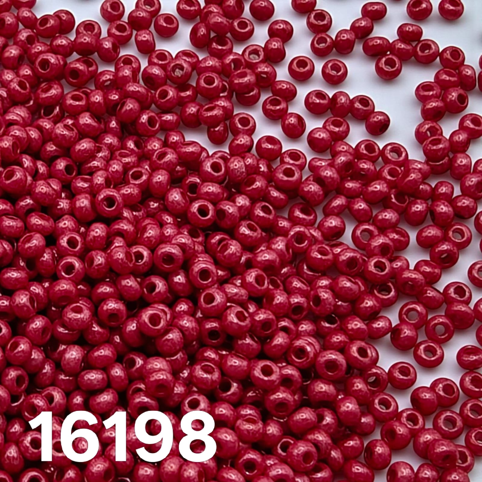Czech seed beads 10/0 Opaque Dyed Chalk Red 16198 scattered on white.