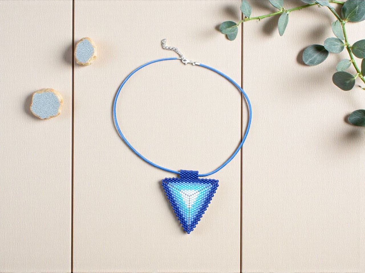 flat lay of blue triangle beaded pendant necklace on beige board with eucalyptus